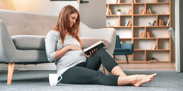 Schwangere Frau sitzt auf dem Boden und liest ein Buch.