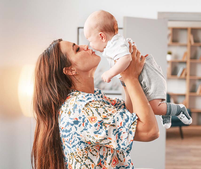 Junge Mutter hält Baby nach oben und küsst es.