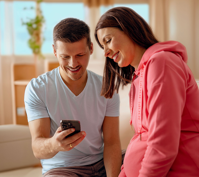 Paar sitzt auf dem Boden und schaut zufrieden auf die Elterngeld Buddy App